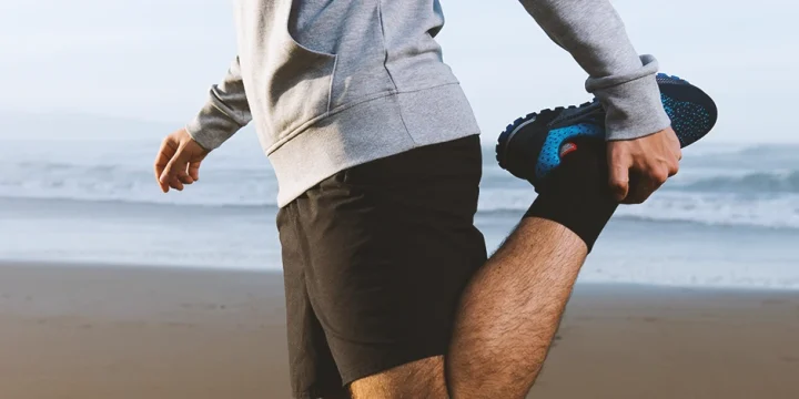 A person doing standing quad stretches at the beach
