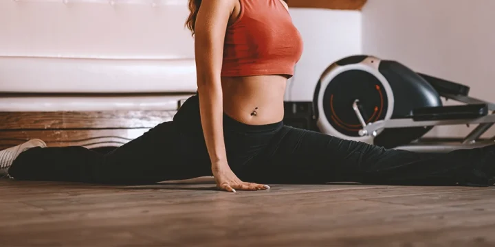A woman at a home gym doing leg splits