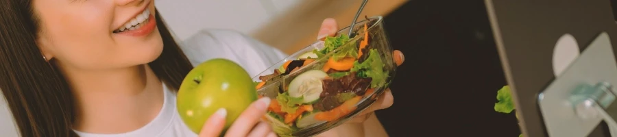 Woman holding a bowl of salad and a apple