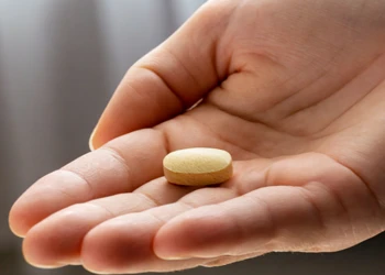 A person's hand holding a piece of vitamin supplement